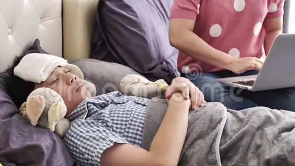 母亲带着一个孩子在家里试着用笔记本电脑工作一个生病的男孩躺在床上视频的预览图