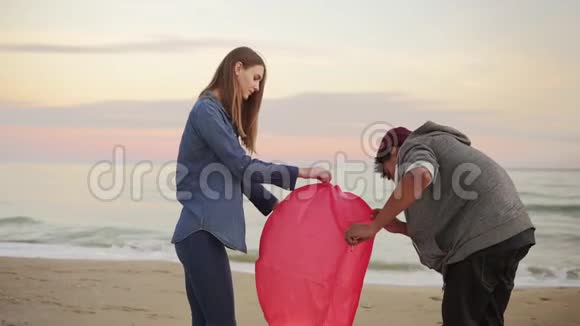 年轻的多民族夫妇在发射前点燃红纸灯笼在海滩上浪漫的约会有魅力的女人视频的预览图