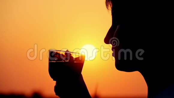 一个美丽的女人在日落背景下喝咖啡特写镜头的缓慢动作视频的预览图