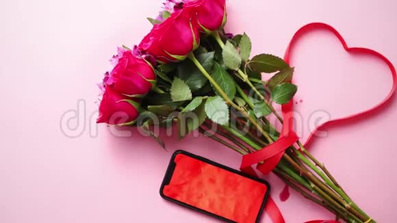 粉红色玫瑰花束与哈特形蝴蝶结手机与复制空间屏幕视频的预览图