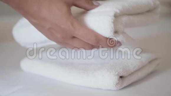 双手特写把一叠新鲜的白色浴巾放在床单上客房服务员清洁酒店客房视频的预览图
