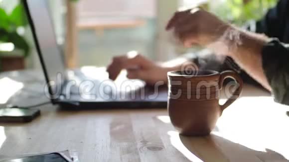 那个人正在笔记本电脑上的桌子上工作他喝热茶把注意力集中在杯子上特写视频的预览图