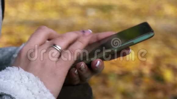 一个女人坐在秋天公园的长椅上在你的手机上输入一条信息视频的预览图