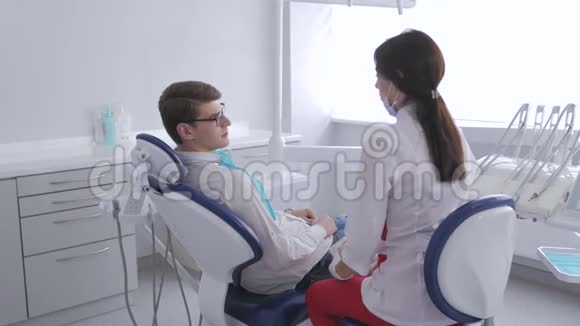 一位女牙医正在和坐在牙科椅上的病人交谈视频的预览图