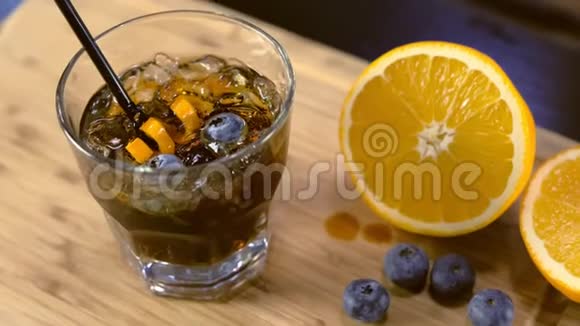 酒精鸡尾酒在岩石玻璃与橙色冰和蓝莓在桌子上侧视视频的预览图