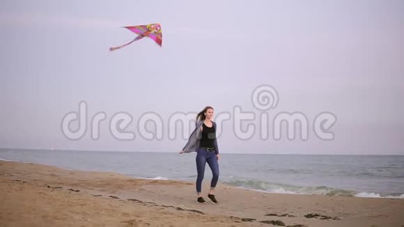 有魅力的年轻女子留着长发在天空中放着五颜六色的风筝晚上在海滩上散步视频的预览图