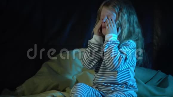 一个晚上穿着条纹睡衣的小女孩坐在床上哭泣视频的预览图