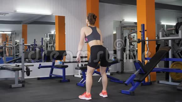 年轻漂亮的运动女孩在健身房里用杠铃表演举重背面观看60英尺视频的预览图
