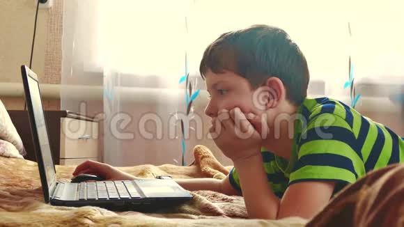 小男孩在卧室里用笔记本玩床室内笔记本电脑上的青少年社交媒体互联网视频的预览图