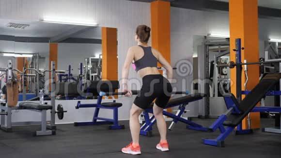 年轻漂亮的运动女孩在健身房里用杠铃做弯曲的排后侧视60fps视频的预览图