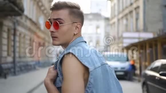 穿着牛仔裤背心和红色太阳镜的人在街上行走时会旋转视频的预览图