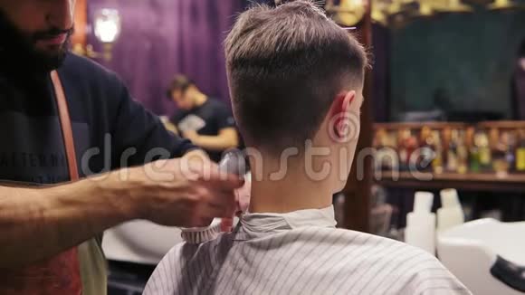 回头看一个客户被理发师剪了头发留胡子的理发师正在用电动理发器理发视频的预览图