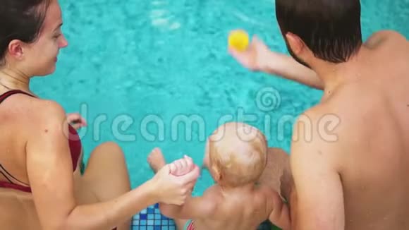 后景年轻的爸爸妈妈抱着孩子在游泳池里跳着手母亲和视频的预览图