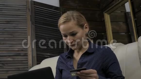 坐在沙发上用笔记本电脑和银行信用卡在线购物的美女慢动作视频的预览图