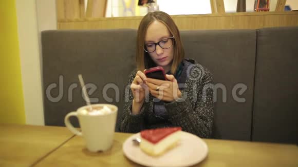 悲伤的女人在咖啡馆里使用智能手机上的应用程序喝着带棉花糖的热巧克力在手机上发短信同时视频的预览图