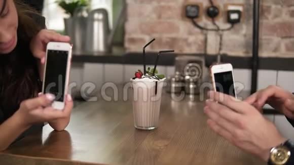 年轻人和女人在咖啡馆的木桌上用奶昔和樱桃和稻草拍一个玻璃杯视频的预览图