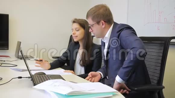 在办公室女人用笔记本电脑向办公桌上的男人解释视频的预览图