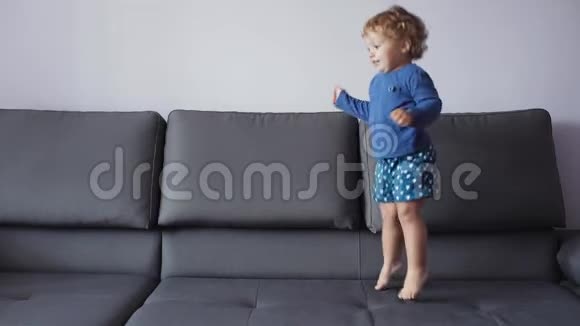金发卷曲的小女孩跳上沙发蓝色的衣服感觉很开心视频的预览图