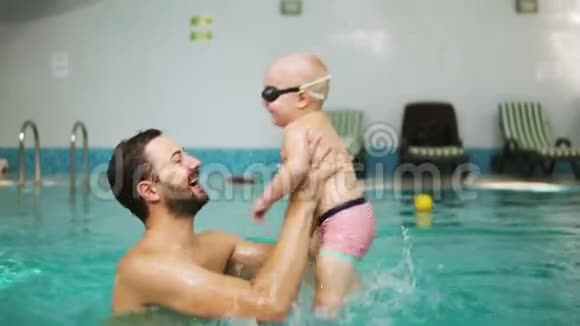 年轻的父亲在教他如何在游泳时把他的小男孩戴着保护眼镜从水中举起视频的预览图