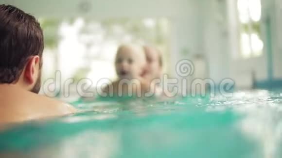 可爱的婴儿和他的母亲和父亲一起上游泳课健康的家庭教孩子游泳视频的预览图