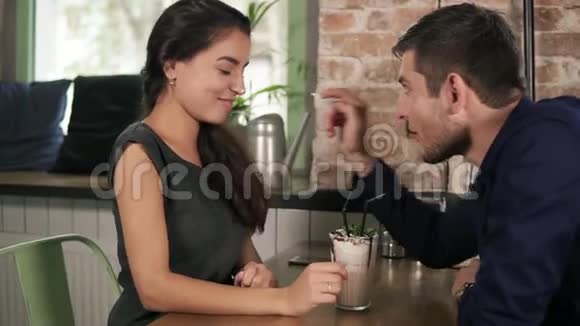 有魅力的一对夫妇在咖啡馆里玩奶昔把鲜奶油涂在对方鼻子上视频的预览图