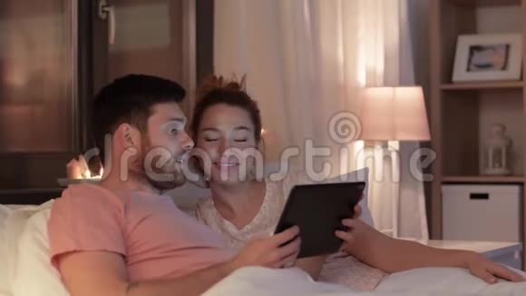 新婚夫妇晚上在床上使用平板电脑视频的预览图