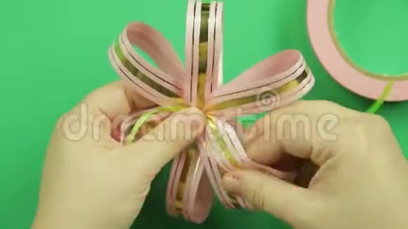 女性的双手在绿色背景上形成粉红色丝带蝴蝶结视频的预览图