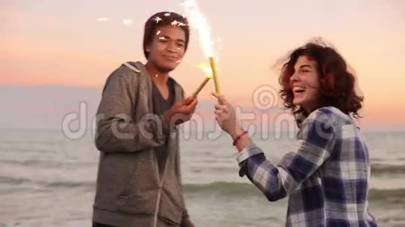 夕阳西下一对多民族的夫妇捧着闪闪发光的蜡烛站在海边视频的预览图