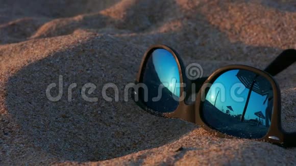 点躺在沙滩上太阳镜里映着太阳天空和那个在海滩上散步的女人一个年轻的女孩视频的预览图