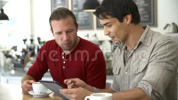 两位男性朋友在咖啡店看数字平板视频的预览图
