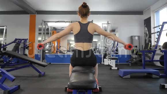运动少女一边做哑铃一边在健身房坐在运动长椅上背面视图60fps视频的预览图
