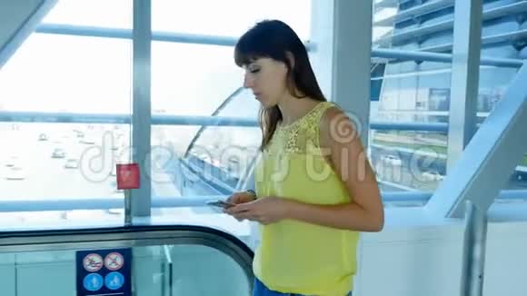 女孩站在地铁道口的自动人行道上用智能手机说话在她身后的窗户上视频的预览图