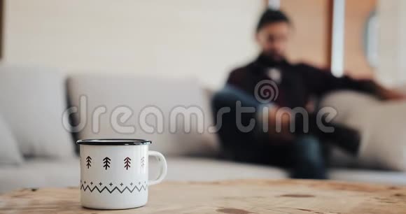 漂亮的胡须男带着智能手机坐在客厅的现代阁楼的沙发上和朋友聊天视频的预览图