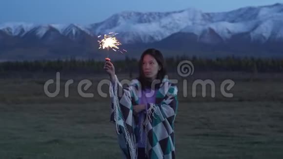 一个穿着毯子的亚洲女孩手里拿着一个闪闪发光的东西日落背景是雪山视频的预览图