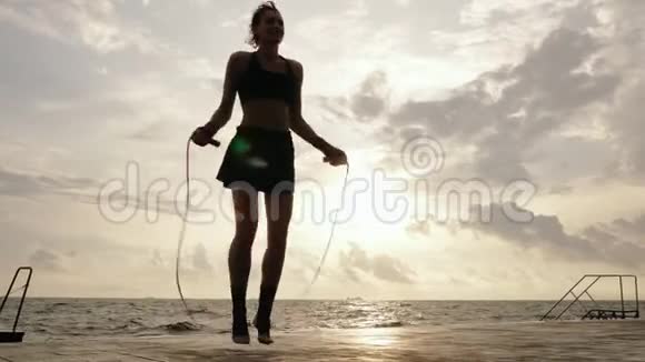 从底部看年轻的女人在海滩边的阳光下慢慢地用跳绳镜头耀斑视频的预览图
