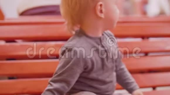 金发幼儿坐在长凳上摔倒试图通过玩具车视频的预览图