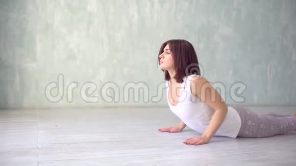 美丽的年轻女子在室内工作在白色墙壁的房间里做瑜伽运动向下面对狗姿势视频的预览图