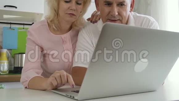 成熟的家庭夫妻在厨房里使用笔记本电脑视频的预览图