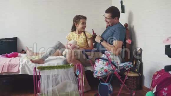 这位年轻的父亲在孩子们的房间里坐在床上用玩具梳子梳女儿爸爸和女儿视频的预览图