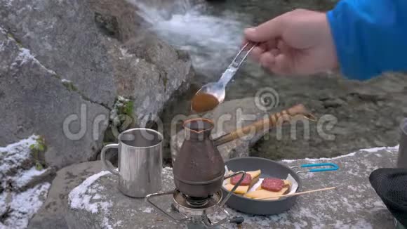 在便携式燃气燃烧器上有一个水壶咖啡被扔进里面山河附近野餐特写视频的预览图