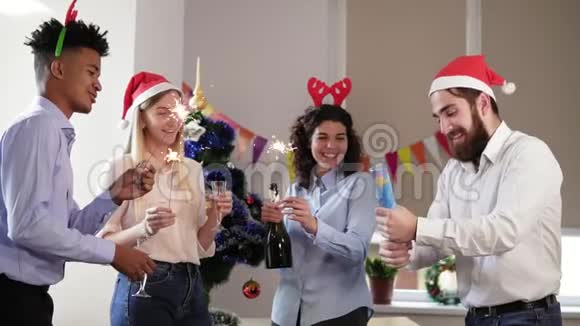 快乐的多民族人士戴着滑稽的帽子在办公室里点燃圣诞和新年的火花兴奋不已视频的预览图
