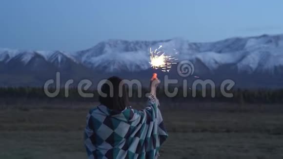 一个穿着毯子的亚洲女孩手里拿着一个闪闪发光的东西日落背景是雪山视频的预览图