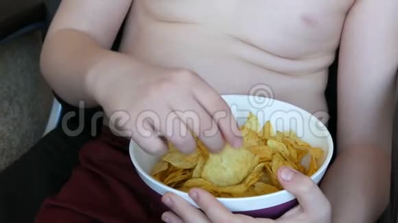 肥胖的少年身体上有着肥胖的褶皱正在用手吃薯片不健康食品快餐儿童视频的预览图