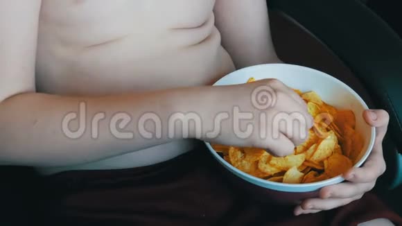 肥胖的少年身体上有着肥胖的褶皱正在用手吃薯片不健康食品快餐儿童视频的预览图
