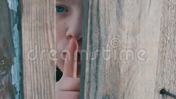 一个被吓呆了的小男孩蓝眼睛透过栅栏或门口的缝隙窥视露出一个手指的痕迹视频的预览图