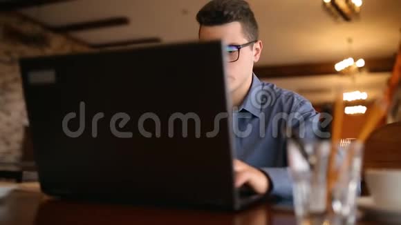 英俊的自由职业者商人戴眼镜勤奋地在咖啡馆的笔记本电脑上工作男子键盘打字和搜索新视频的预览图