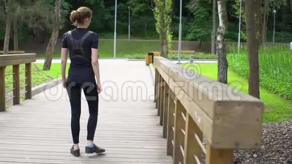 有魅力的健身女人在木桥上伸展腿在公园里锻炼慢动作视频的预览图