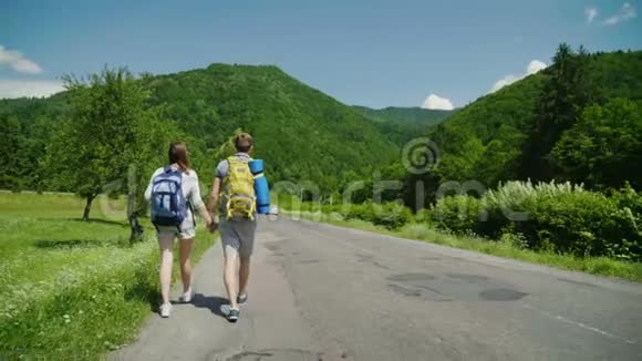 几个带背包的游客手牵着手在一个风景如画的地方沿着马路散步后视图视频的预览图
