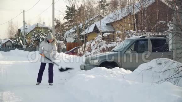 年轻女子在冬天用铁锹给郊区的汽车擦雪视频的预览图