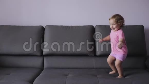金发卷曲的小女孩跳上沙发蓝色的衣服感觉很开心慢动作视频的预览图